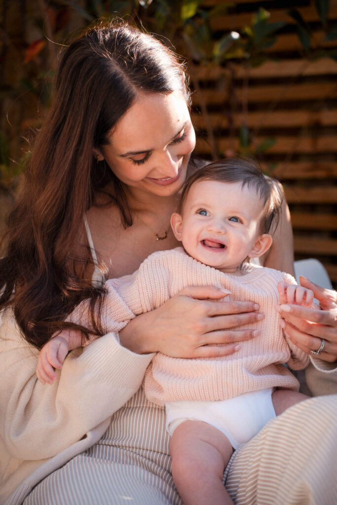 Candid moment of a mother smiling at her laughing baby during an outdoor family photography session in Munich. An example of why mothers need to be in the frame.
